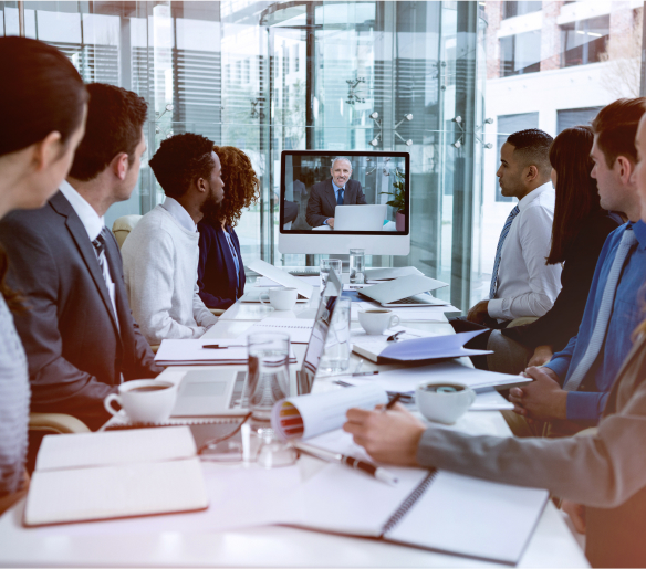 A group of people sitting at a conference table watching a video conference.